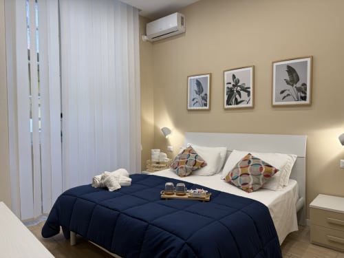 Camera moderna all'Hotel Encanto Naples con letto bianco, piumone trapuntato blu navy, arte botanica alle pareti e vista sulla città