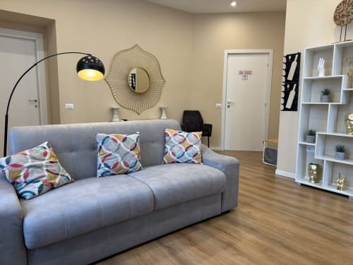 Soggiorno moderno dell'Encanto Hotel di Napoli con divano grigio, cuscini colorati, lampada ad arco e scaffali bianchi