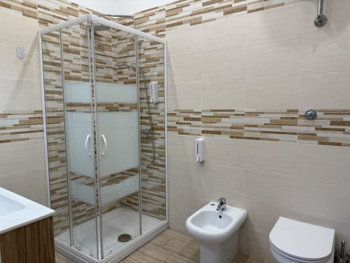 Bagno moderno all'Encanto Hotel di Napoli con doccia in piastrelle a righe, sanitari bianchi e design contemporaneo