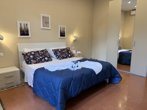 Camera da letto dell'hotel Encanto a Napoli con letto matrimoniale, cuscini floreali, coperta blu e servizi moderni