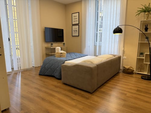 Camera moderna dell'Hotel Encanto Naples con letto, TV, lampada ad arco, pavimento in legno e vista città dalle finestre a tutta altezza