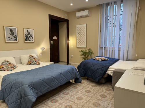 Camera doppia moderna dell'hotel Encanto Napoli con vista sulla città, trapunte blu, pareti gialle e arredamento contemporaneo
