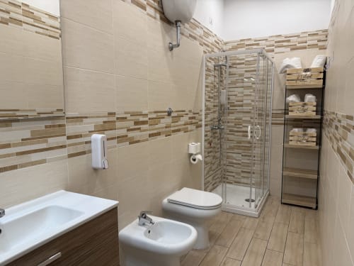 Bagno moderno dell'Hotel Encanto Naples con doccia, wc, bidet e rivestimenti in gres porcellanato effetto legno
