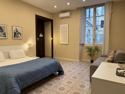 Camera da letto dell'hotel Encanto a Napoli con vista sulla città, piumone blu, pareti gialle e arredamento moderno