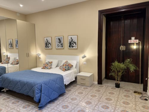 Camera moderna dell'Hotel Encanto Naples con letto trapuntato blu, guardaroba specchiato e opere botaniche