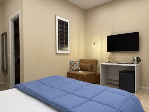 Camera moderna all'Encanto Naples con letto blu, poltrona marrone, TV a parete e vista sulla città