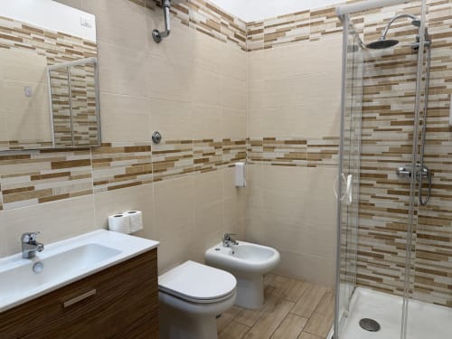 Bagno moderno all'Encanto Hotel Naples con piastrelle a righe, doccia aperta, sanitari bianchi e vanity in legno