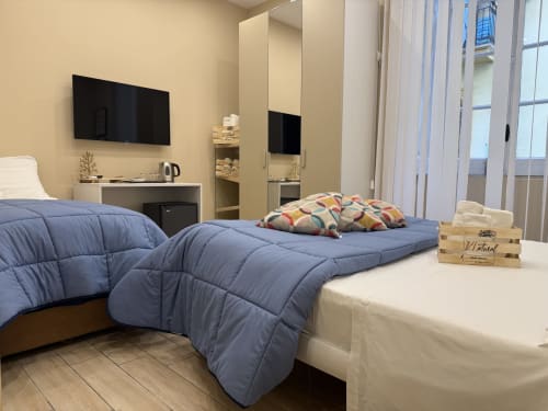 Camera d'hotel Encanto a Napoli con letto blu, scrivania, TV e vista sulla città dal balcone