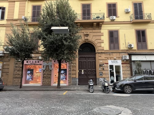 Facciata dell'Encanto Hotel a Napoli con vetrine colorate, ingresso ricoperto di edera, balconate e scooter parcheggiati in strada