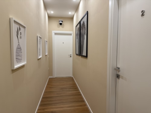 Corridoio moderno dell'hotel Encanto a Napoli con pavimenti in legno, pareti color crema, quadri incorniciati e porte bianche verso le camere