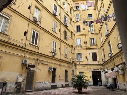 Cortile dell'Encanto Hotel a Napoli con edifici gialli, finestre, stenditoio e palma centrale