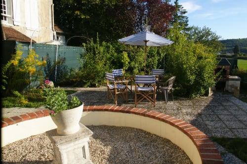 Charming garden patio at Les Gîtes de l'Impériale B&B in Sermizelles with striped umbrella, seating area, and brick-edged