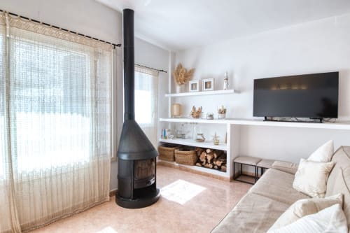 Salon moderne avec cheminée suspendue noire, étagères blanches, TV, canapé beige et lumière naturelle chez Finques Garcia