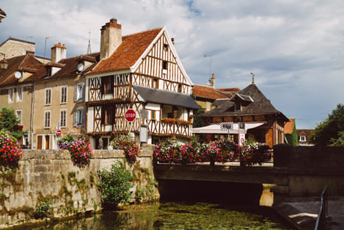 Half-timbered medieval buildings with red flowers along a canal bridge in Sermizelles, France at Les Gîtes de l'Impériale B&B