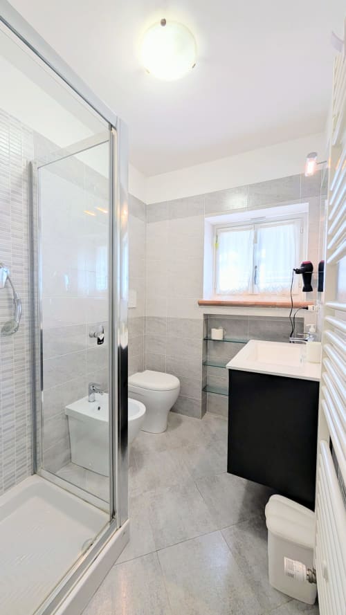 Modern bathroom in Italian villa with black vanity, glass shower enclosure, and gray tile flooring