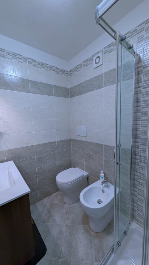 Bagno moderno con piastrelle grigie e bianche, WC, bidet e doccia in vetro alla Villa Italia Management