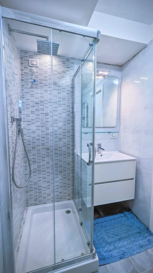 Bagno moderno con box doccia in vetro, piastrelle grigie a mosaico, vanity bianca e tappetino blu a Villa Italia sul lago