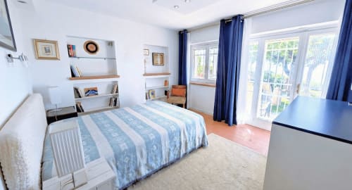 Camera da letto luminosa con biancheria a righe blu, vista lago, scaffali in legno, tende blu e pavimento in cotto a Villa Italia