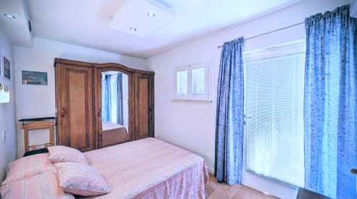 Camera da letto luminosa con biancheria rosa, armadio in legno, tende blu e porte in vetro nella villa sul lago italiano