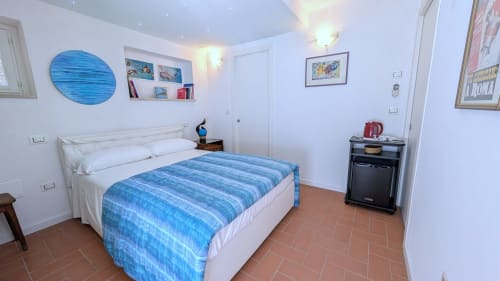 Camera da letto luminosa con biancheria blu rigata, pareti bianche, pavimento in terracotta e vista sul lago presso Villa Italia Management