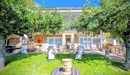 Giardino del Lago Villa Italia con prato, zone lounge ombreggiate, casa in pietra con persiane blu e vasca idromassaggio