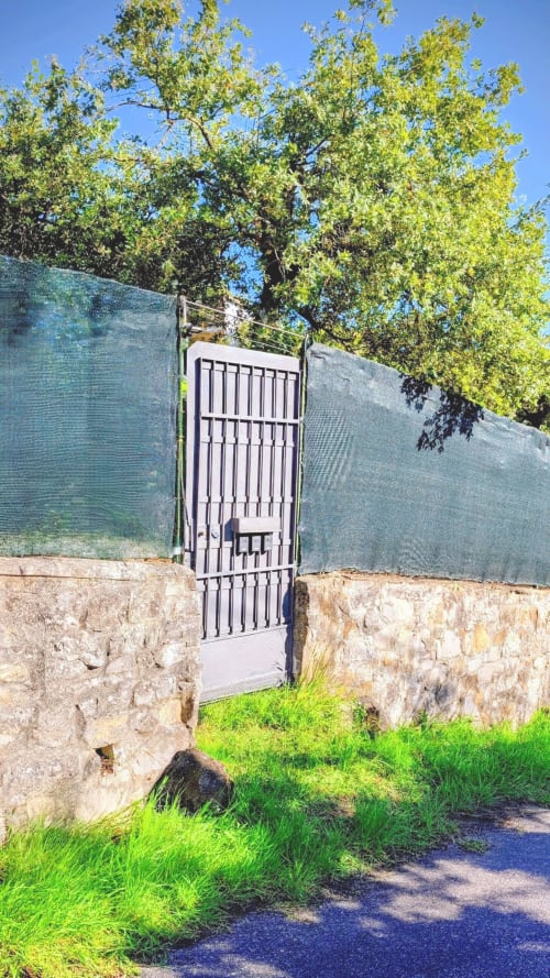 Cancello d'ingresso villa in pietra con giardino rigoglioso e vista lago, proprietà italiana