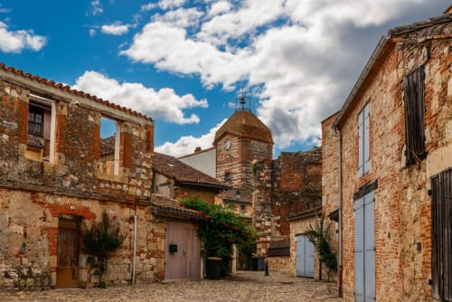 Cour historique en pierre de la maison d'hôtes Alombre à Lectoure, avec bâtiments en terre cuite et clocher