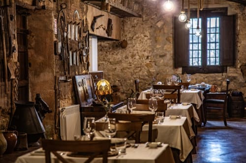 Interior rústico de piedra del restaurante Masia Can Canyes con mesas dispuestas, decoración vintage e iluminación cálida en Sant Llorenç