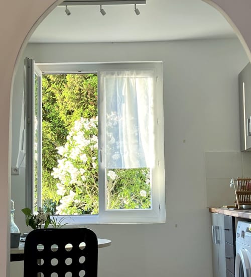 Fenêtre lumineuse de la chambre de l'hôtel Accolade à Châteaudun donnant sur un jardin verdoyant avec fleurs blanches