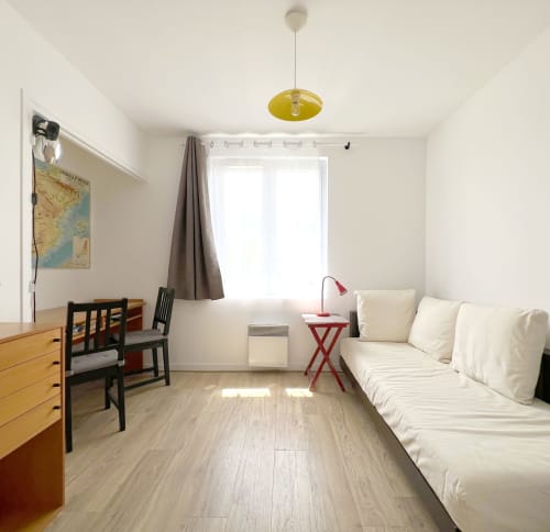 Chambre lumineuse de l'hôtel Accolade à Châteaudun avec canapé crème, bureau en bois et suspension jaune