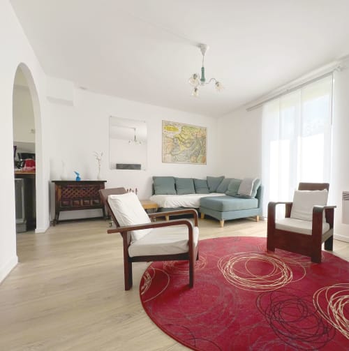 Salon de cottage moderne à l'Accolade à Châteaudun avec canapé vert, mobilier en bois et tapis à motifs rouges