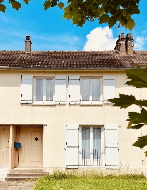 Cottage Accolade à Châteaudun avec façade crème, fenêtres volets, toit de tuiles et canopée d'arbres