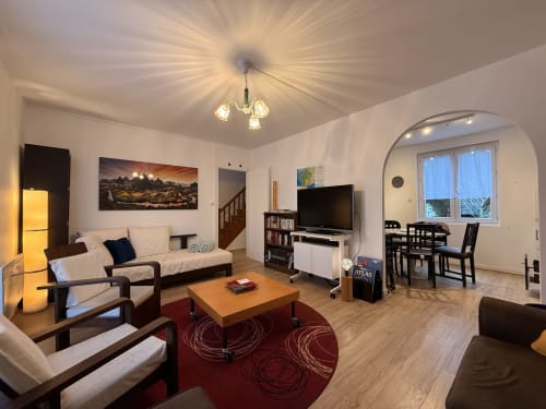 Spacieux espace de vie ouvert au gîte Accolade à Châteaudun avec canapé crème, mobilier en bois, tapis rouge et coin repas.