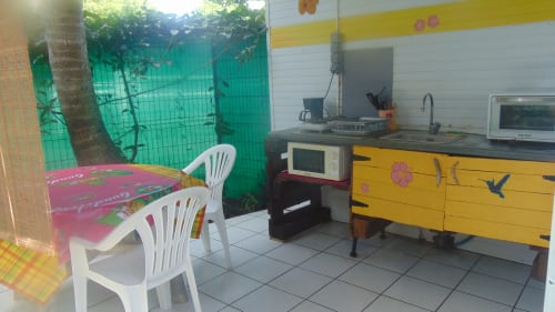 Cuisine du cottage Caribgites à Sainte-Anne avec armoires jaunes, chaises blanches et vue sur le jardin à travers un voilage vert