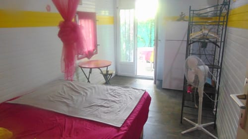Chambre de cottage aux teintes rose et jaune chez Caribgites avec lit, ventilateur et portes sur jardin à Sainte-Anne, Guadeloupe