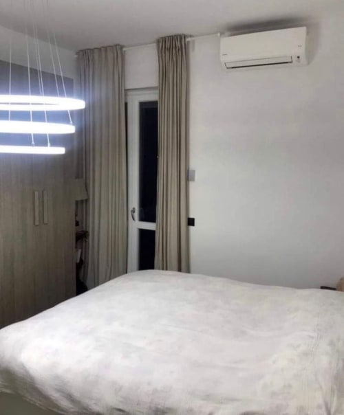Modernes Schlafzimmer in den Magnolia Apartments Mailand mit weißem Bett, beigen Vorhängen, Klimaanlage und Stadtblick