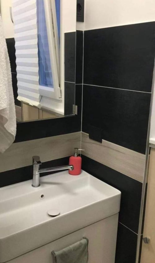 Modernes Badezimmer im Magnolia Apartments Milan mit weißem Waschbecken, Spiegel, schwarzen Wandfliesen und rotem Seifenspender