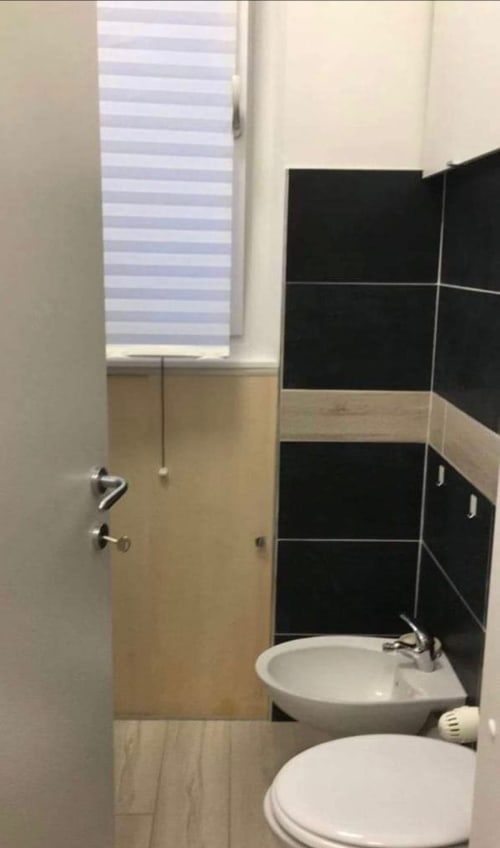 Modernes Badezimmer in den Magnolia Apartments Mailand mit weißem Waschbecken, Toilette, schwarzen Fliesenwänden und Fenster mit Jalousien