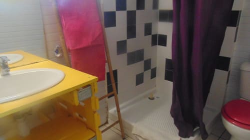 Élégant lavabo jaune éclatant avec vasque blanche, carrelage de douche à carreaux noir et blanc, serviettes rouges et violettes à Caribgites