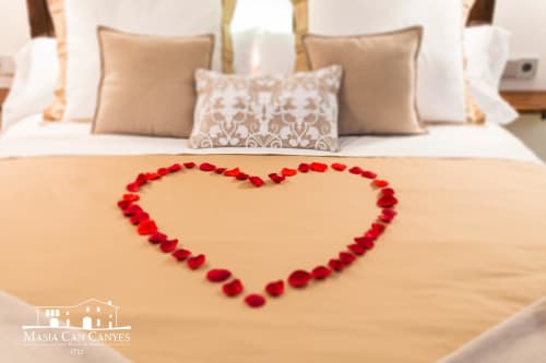 Pétalos de rosa roja dispuestos en forma de corazón en la cama del hotel Masia Can Canyes, Sant Llorenç d'Hortóns