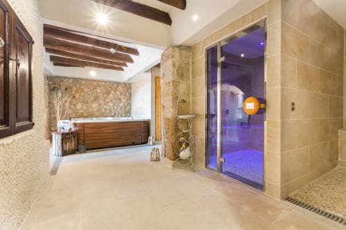 Espace spa luxueux à Masia Can Canyes avec plafond à poutres apparentes, accents en pierre, baignoire en bois et entrée de hammam vitrée