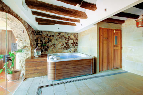 Luxueux bain à remous intérieur à la Masia Can Canyes avec poutres en bois, murs en pierre et installations spa à Sant Llorenç d'Hortóns