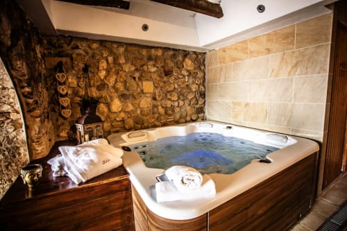 Luxueux bain à remous aux eaux bleues à l'hôtel Masia Can Canyes, avec murs en pierre rustique et touches de bois à Sant Llorenç
