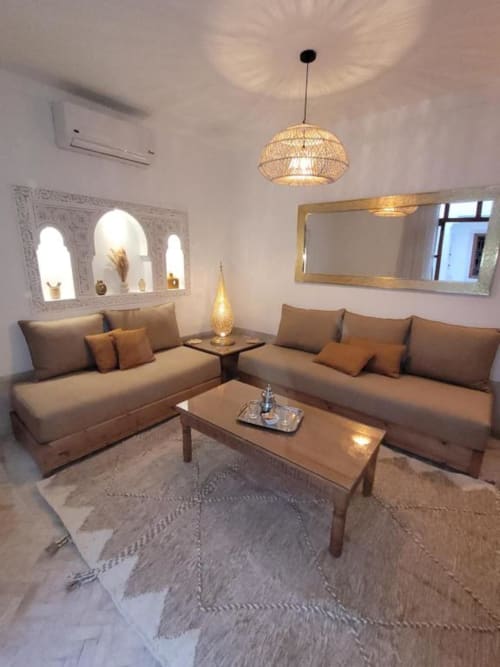 Salon luxueux du Riad Casa Angelo à Marrakech, avec canapés beiges, suspension en tissage et niches murales décoratives.