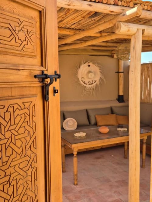 Les portes en bois sculpté du Riad Casa Angelo s'ouvrent sur un salon cosy de Marrakech aux plafonds à poutres et sièges moelleux