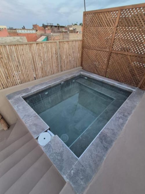 Piscine immergée sur la terrasse du toit du Riad Casa Angelo à Marrakech, avec écrans de confidentialité ajourés et vue sur la ville