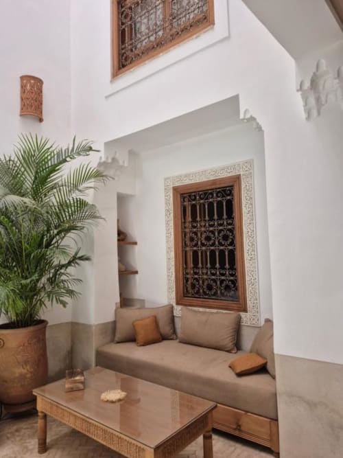 Salon de riad marocain avec canapé taupe, porte en bois ouvragé, palmier et décoration murale traditionnelle au Riad Casa Angelo