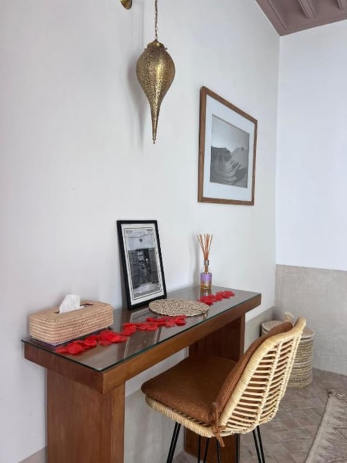 Bureau de riad à Marrakech avec chaise tressée, lampe suspension en laiton, œuvre encadrée et pétales de rose rouge dans la Suite Jamal