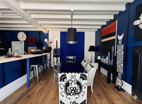 Salon Alombre BnB aux murs bleu vif, poutres blanches, luminaire suspendu noir moderne et décoration éclectique noir et blanc