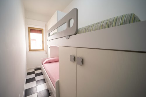 Camera da letto compatta con letto a castello, materasso rigato, armadi contenitori e pavimento a scacchiera nell'appartamento spiaggia di Marina di Strongoli